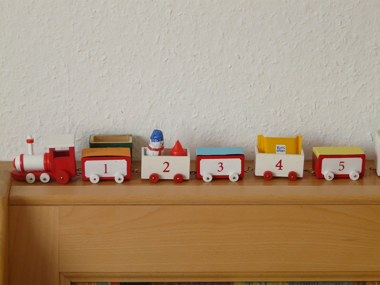menu-03 Red and white wooden toy train with numbers displayed on a wooden shelf.