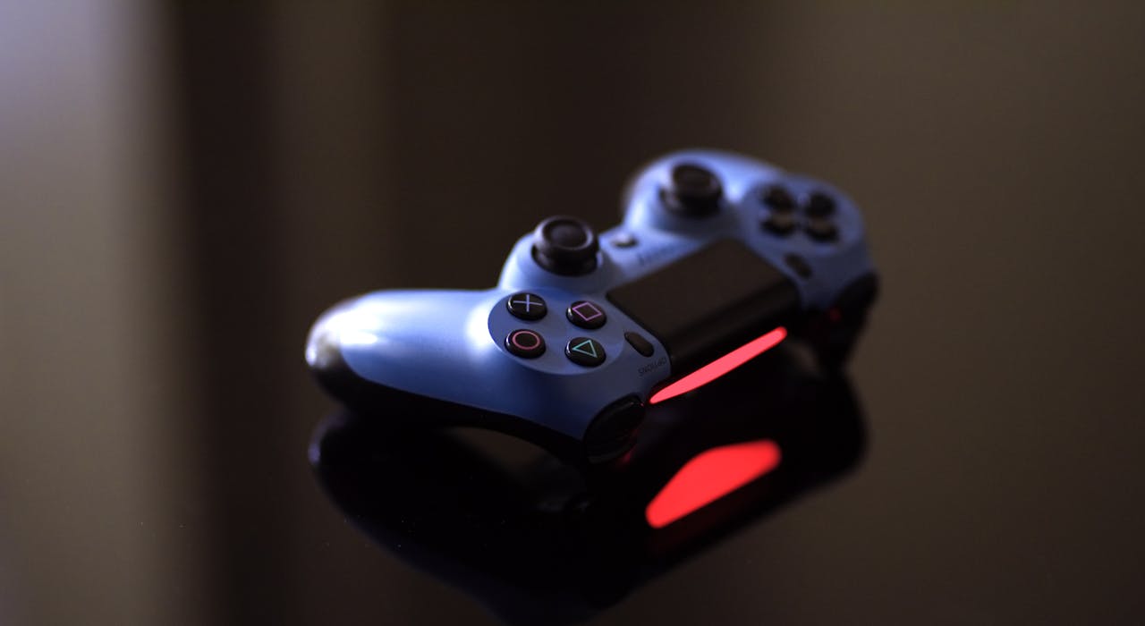 menu-12 Close-up of a blue PlayStation controller on a glossy black surface with red lighting.