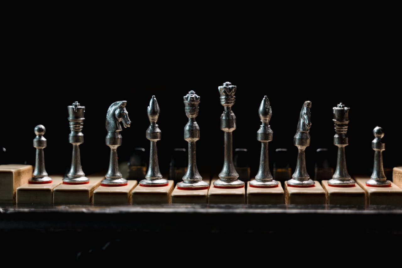 menu-04 A row of elegant metal chess pieces displayed on wooden blocks against a dark background.