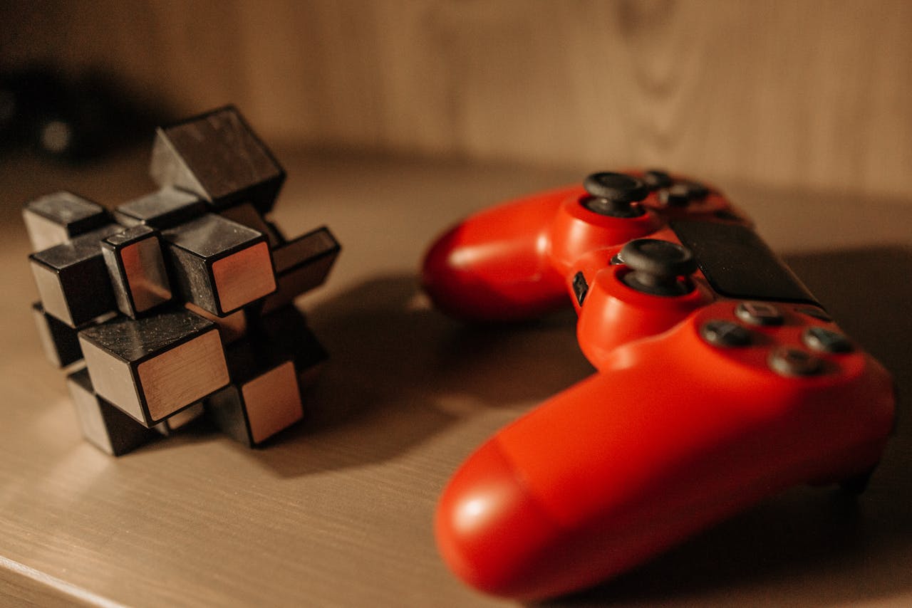 menu-05 Close-up of a red game controller and 3D cube puzzle on a wooden surface.
